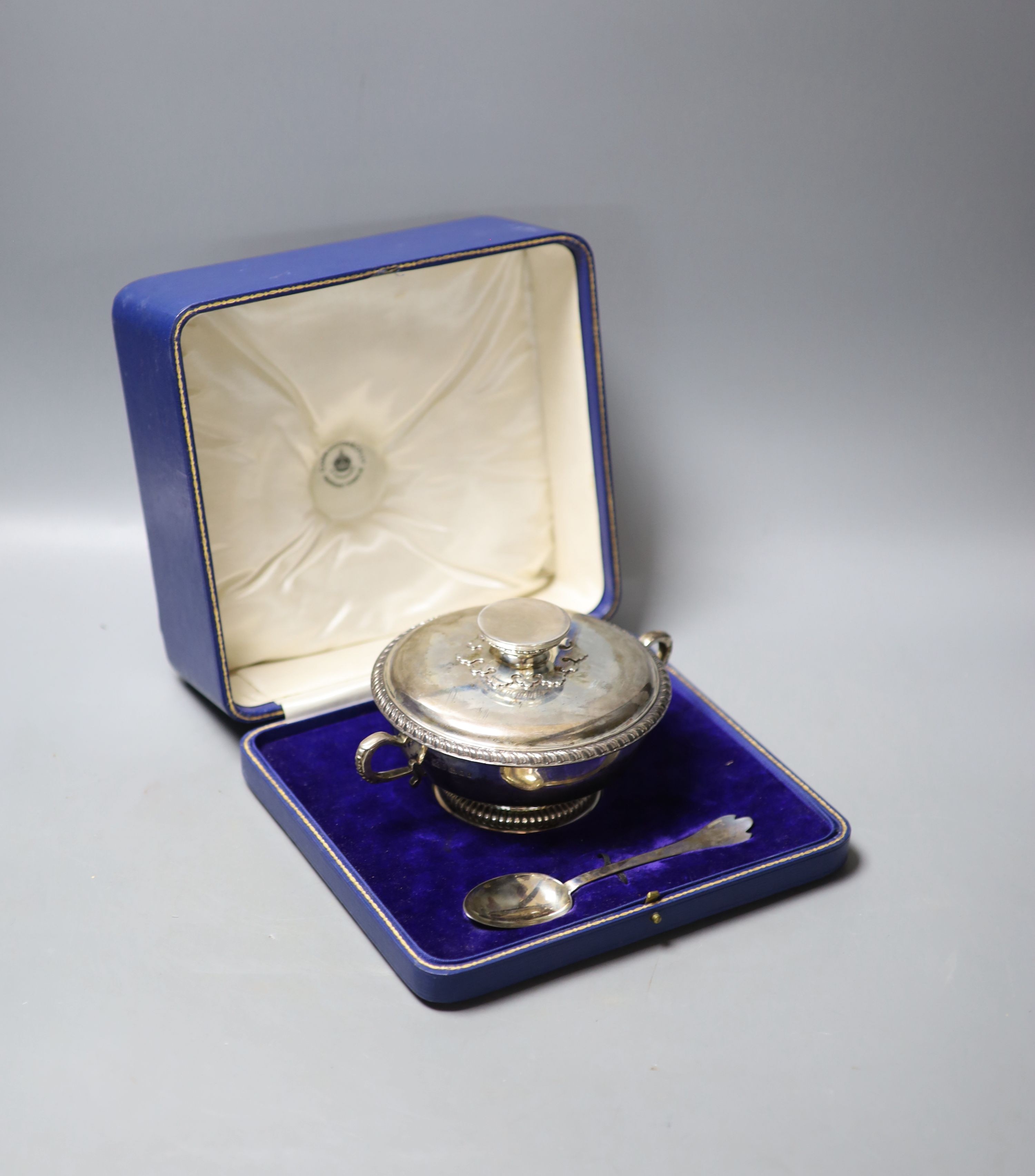 A cased George V silver porringer cup and cover, Carrington & Co, London, 1924, diameter 18.3cm, together with a rat tail trefid spoon, Francis Higgins & Sons Ltd, London, 1924, 170z.